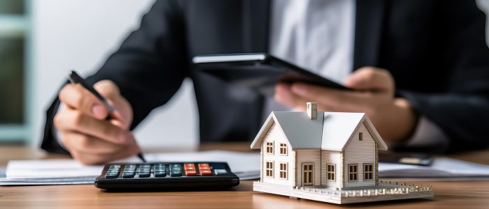 Eine Person kalkuliert Finanzen an einem Tisch mit Modellhaus und Taschenrechner