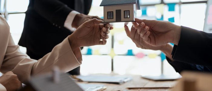 Mehrere Personen mit Vorkaufsrecht halten ein Modellhaus über einem Tisch