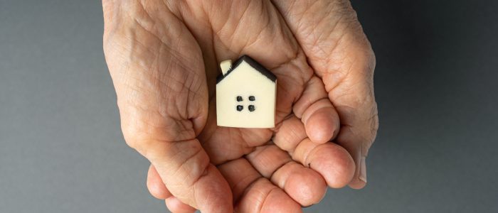 in offenen Händen eines älteren Menschen liegt ein Modellhaus