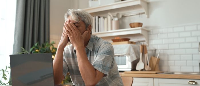 Man sitzt am Computer in der Küche und hält sich die Hände vor sein Gesicht
