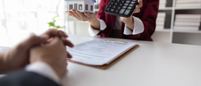 Geschäftsfrau hält ein Modellhaus und einen Taschenrechner in ihren Händen